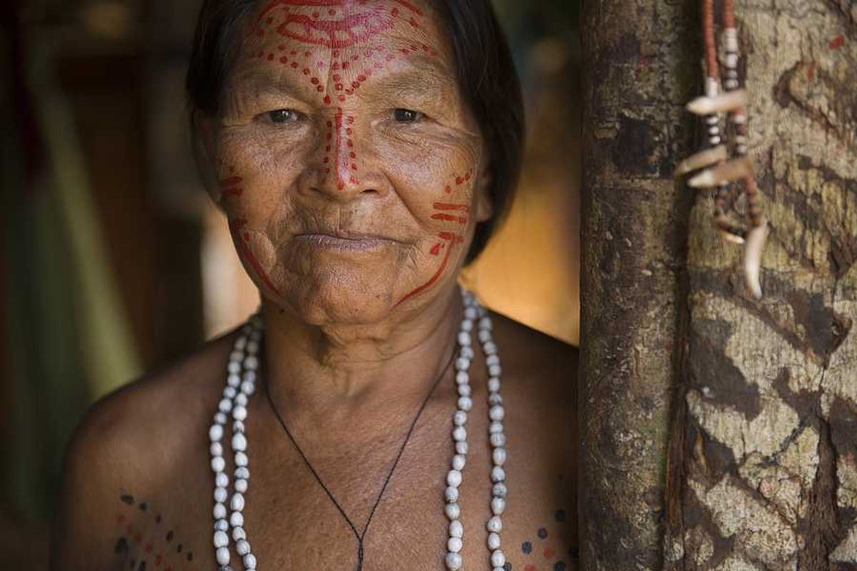 An indigenous woman with red paint on her face standing next to a tree