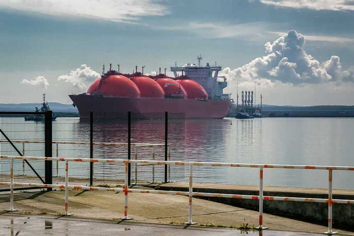 An LNG tanker ship and tugs are maneuvering for docking at a gas terminal