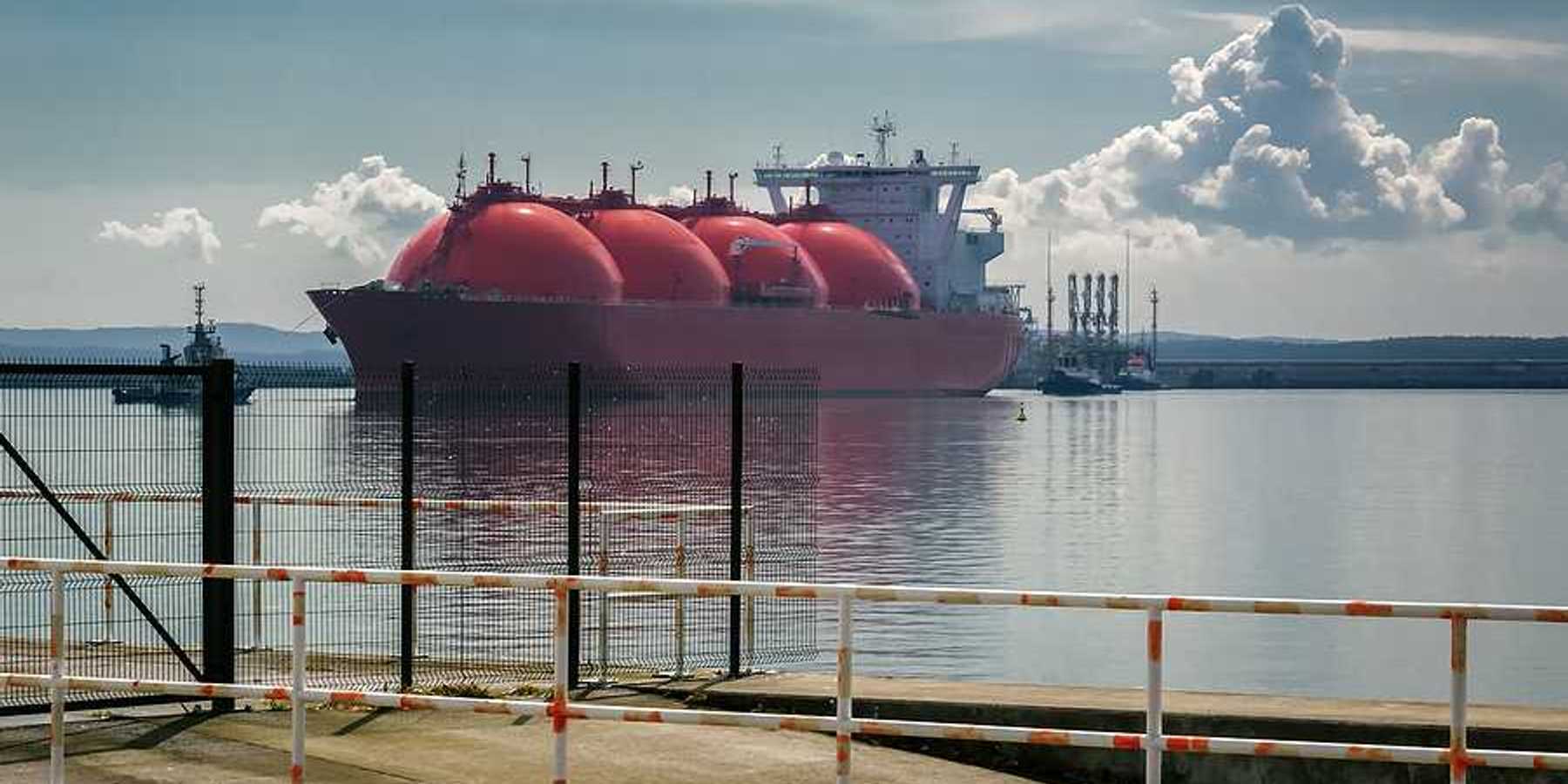 An LNG tanker ship and tugs are maneuvering for docking at a gas terminal