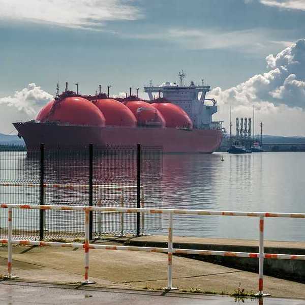 An LNG tanker ship and tugs are maneuvering for docking at a gas terminal
