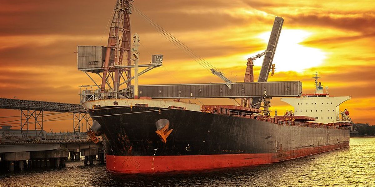An ocean-going vessel at a dock with golden sun and clouds in background.