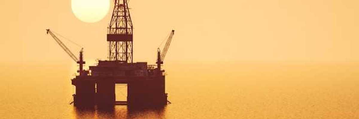 An offshore oil platform with the sun setting in the background