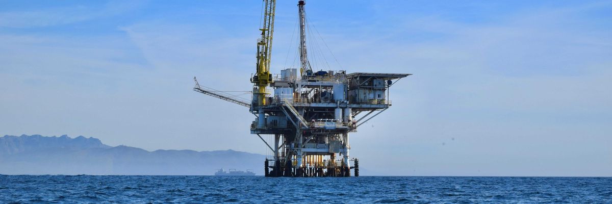 An offshore oil rig in the ocean with mountains in the background