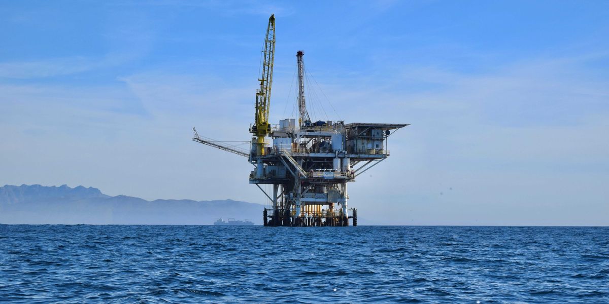 An offshore oil rig in the ocean with mountains in the background