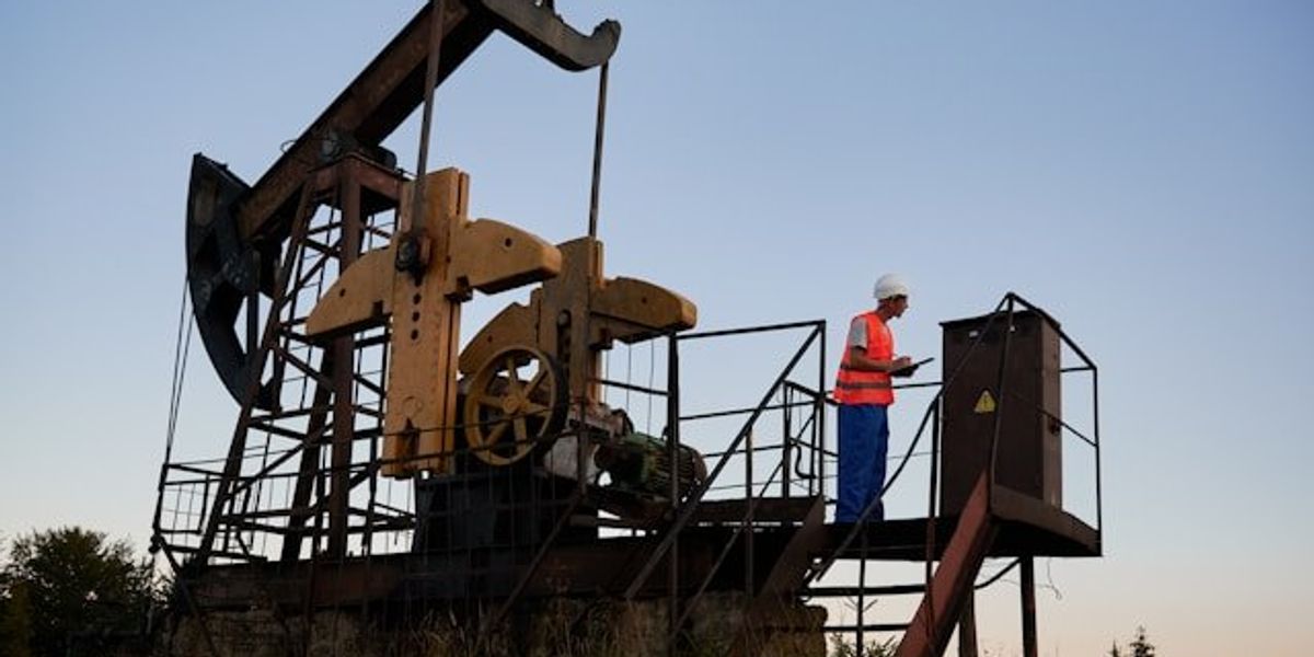 An oil derrick with an oil worker in an orange safety vest.