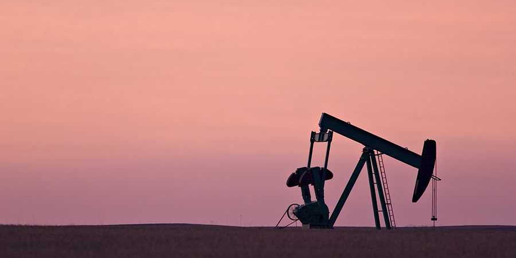 An oil drill pump jack against a sunset sky