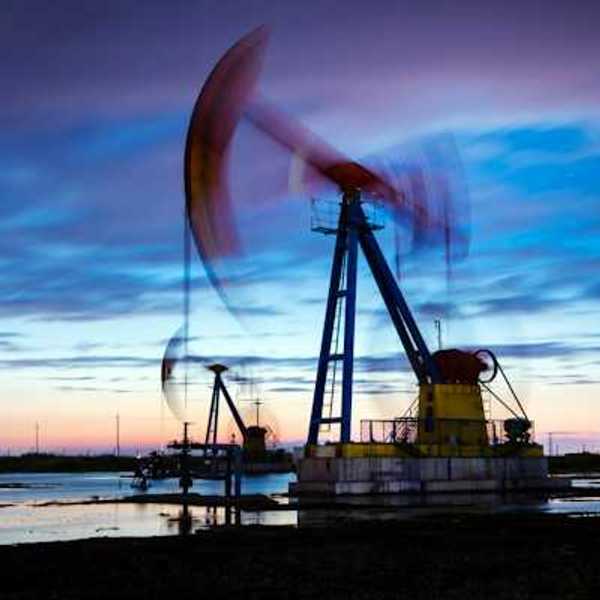 An oil drilling pump jack working in a field a dusk