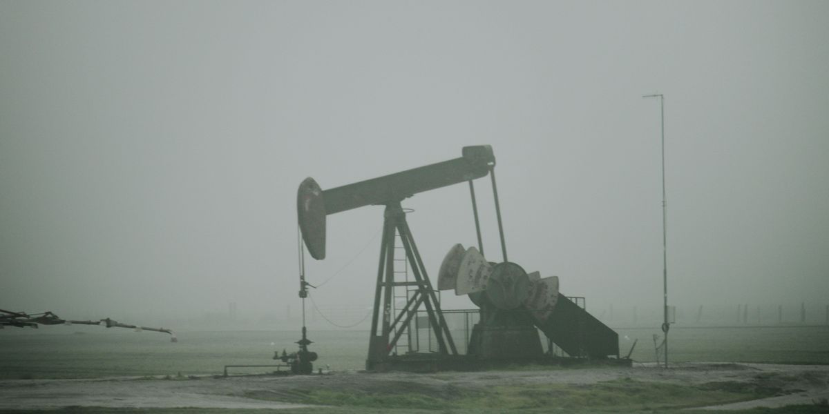 an oil pump in the middle of a field on a rainy, misty day.