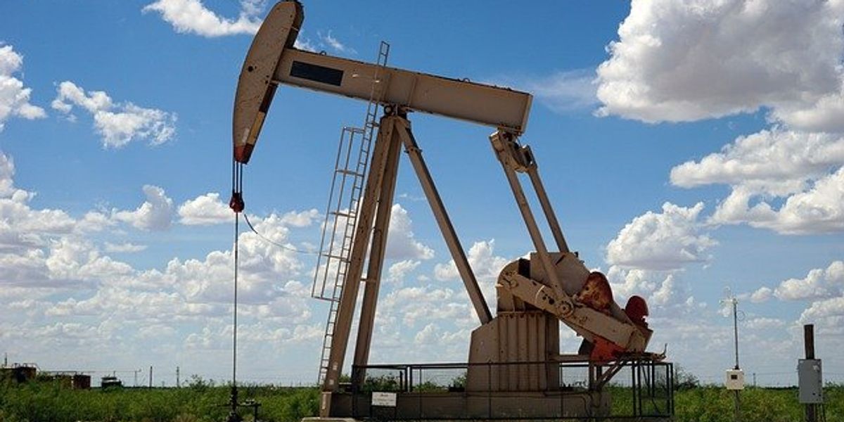 An oil pump jack in a dry field on a sunny day with distant clouds.