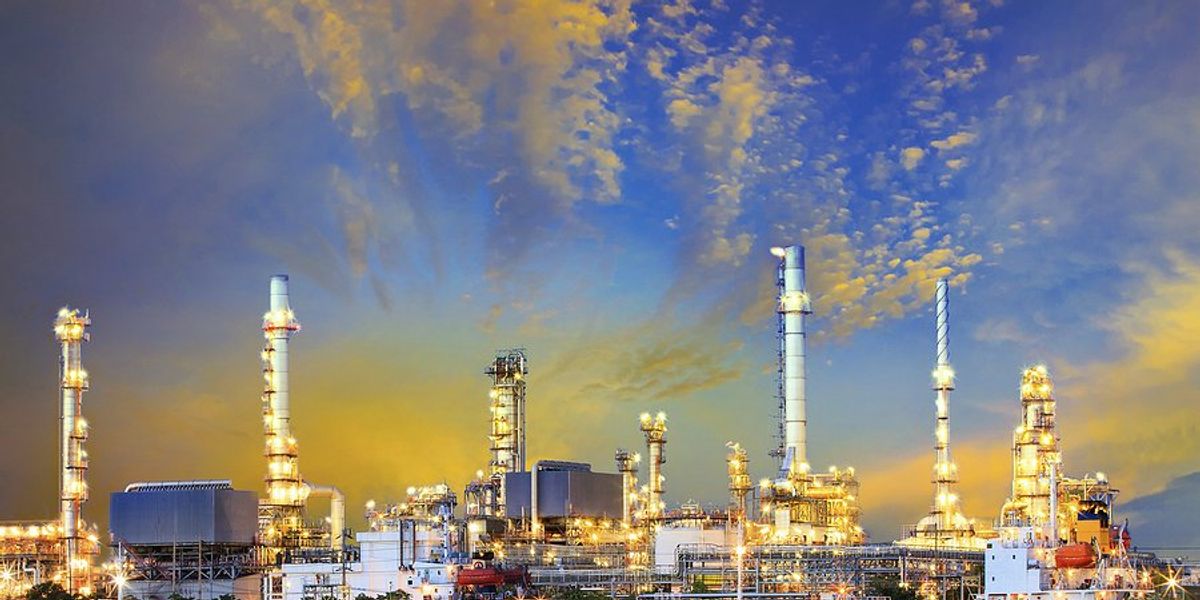 An oil refinery next to a body of water with tankers docked nearby.