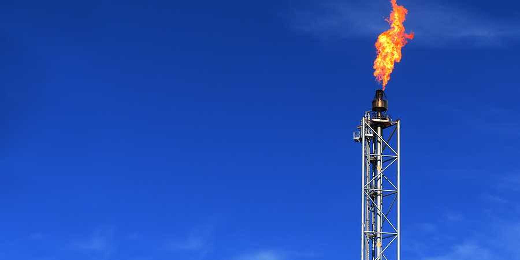 An oil tower with flames during a gas flare against a blue sky