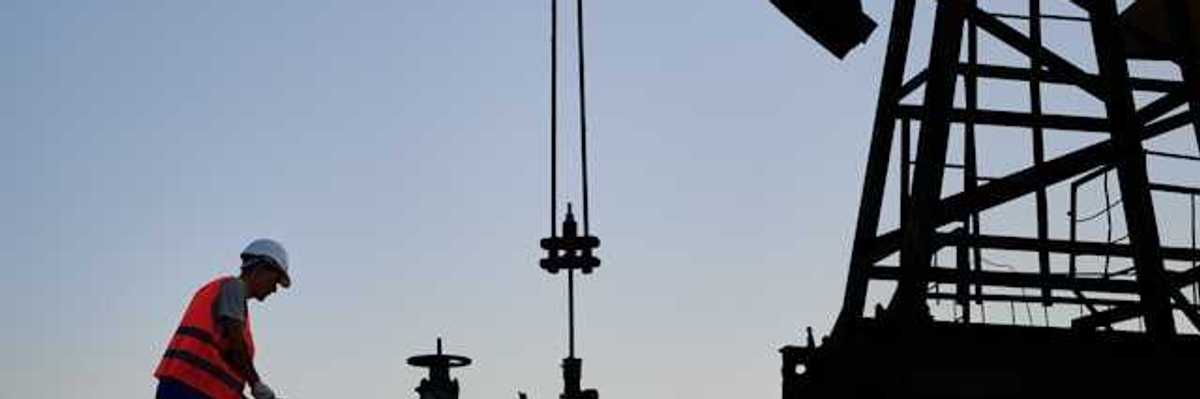 An oil worker at dusk next to a pump jack