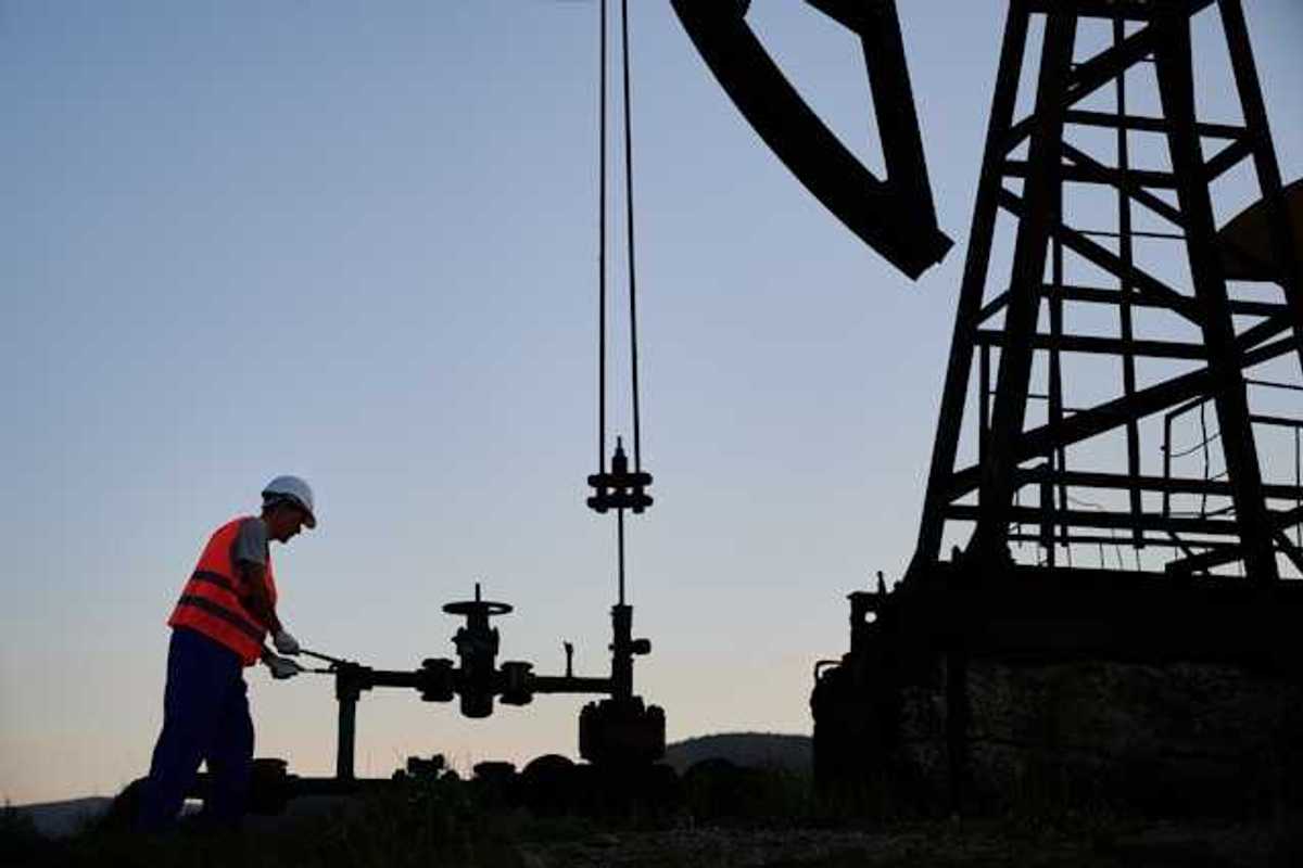 An oil worker at dusk next to a pump jack