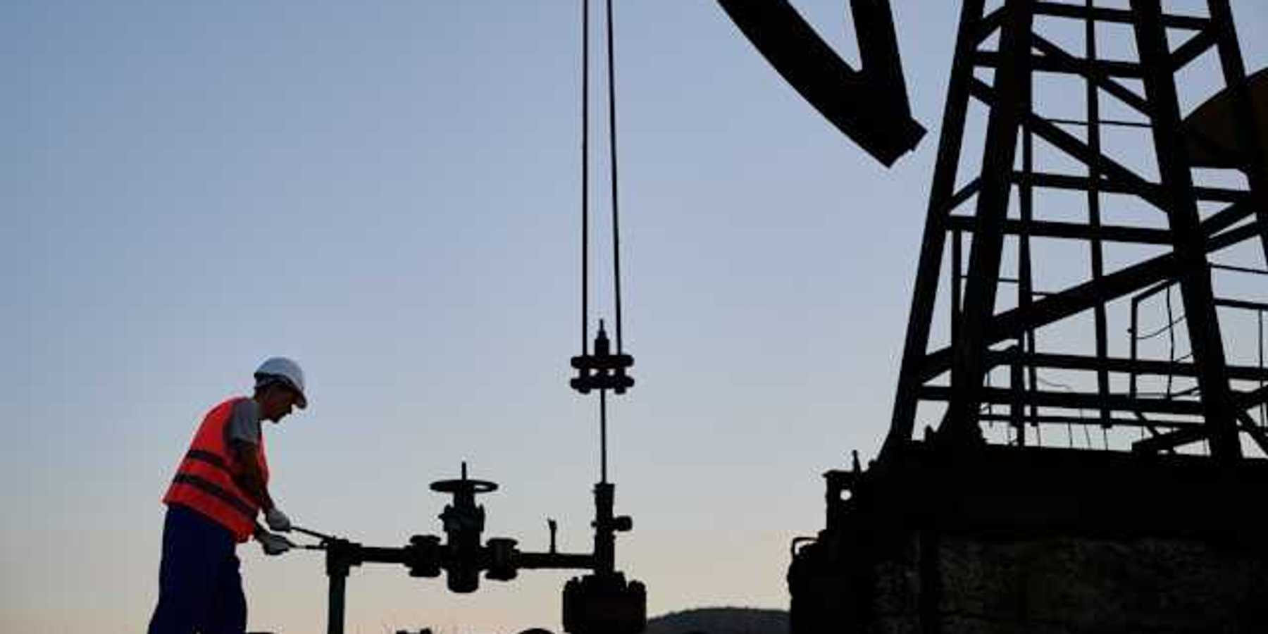 An oil worker at dusk next to a pump jack