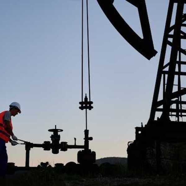 An oil worker at dusk next to a pump jack