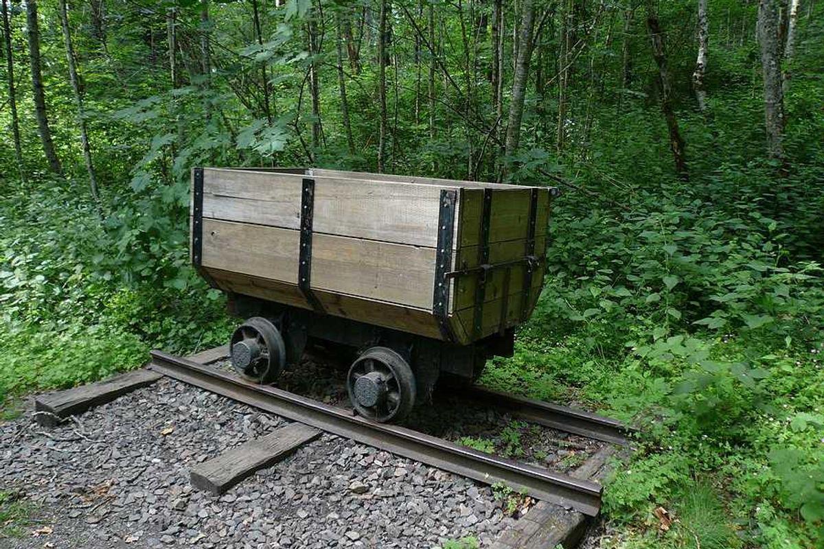 An old wooden mining cart on a rusty set of tracks with a green forest in the background