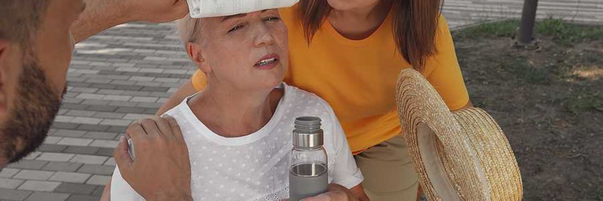 An older woman with a bottle of water being taken care of by two other people during a heat wave