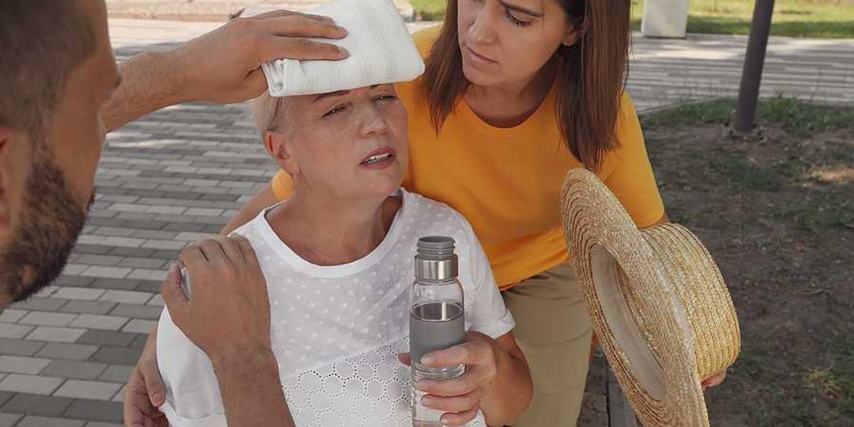 An older woman with a bottle of water being taken care of by two other people during a heat wave
