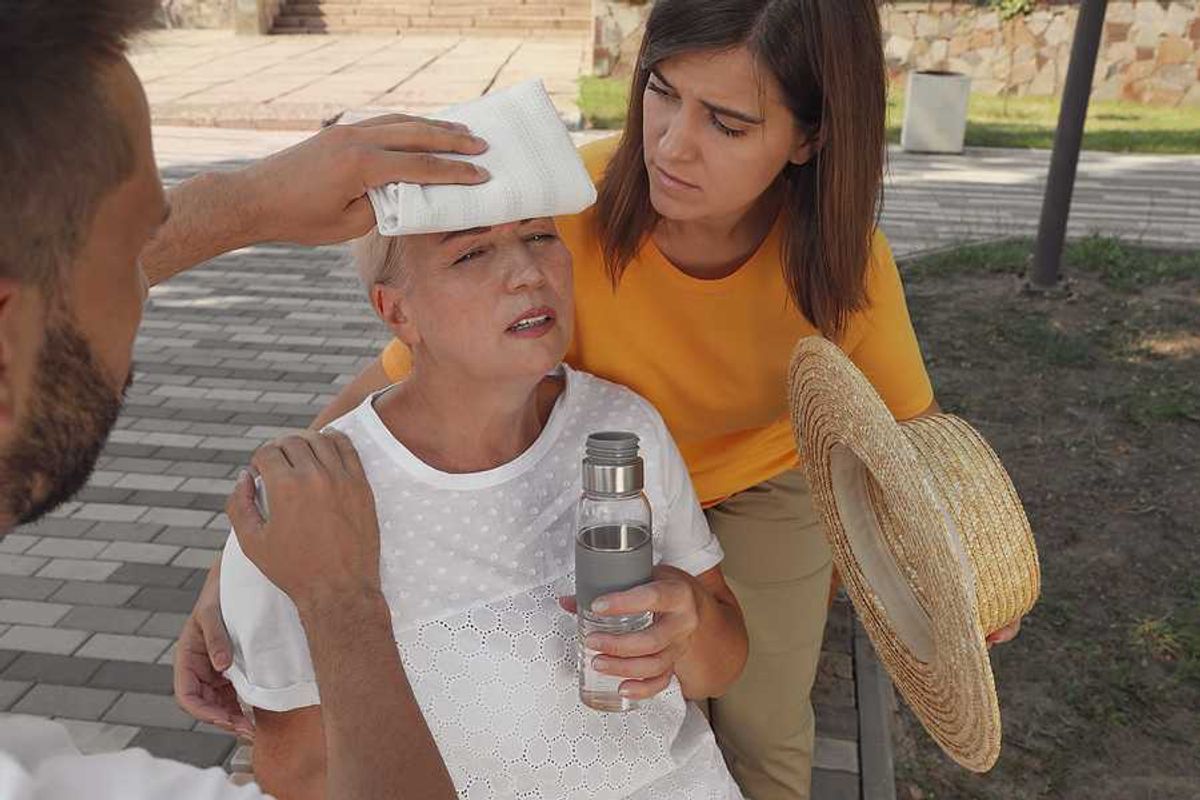 An older woman with a bottle of water being taken care of by two other people during a heat wave