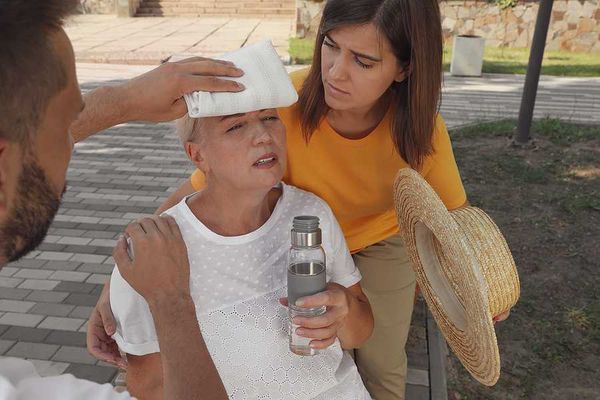 An older woman with a bottle of water being taken care of by two other people during a heat wave