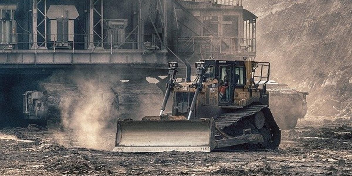 An open pit mine with dust kicked up by equipment and a processing building in the background.