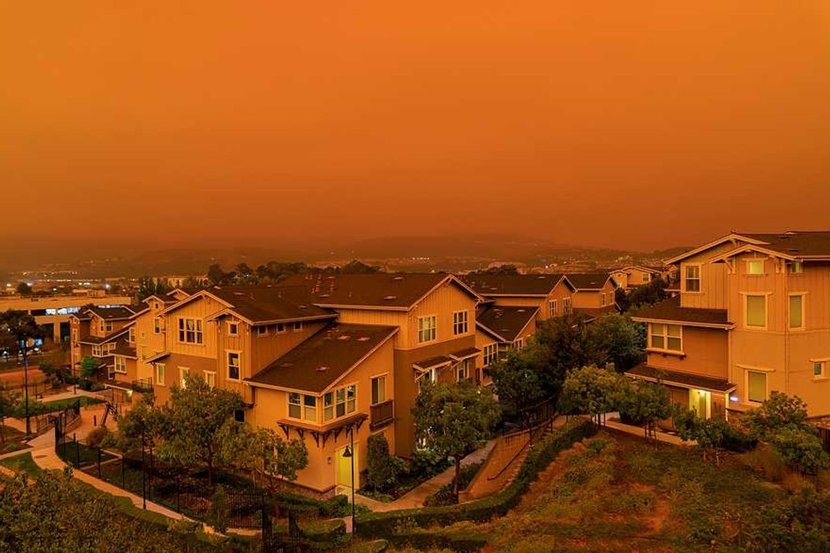 An orange-tinged sky and houses during a wildfire