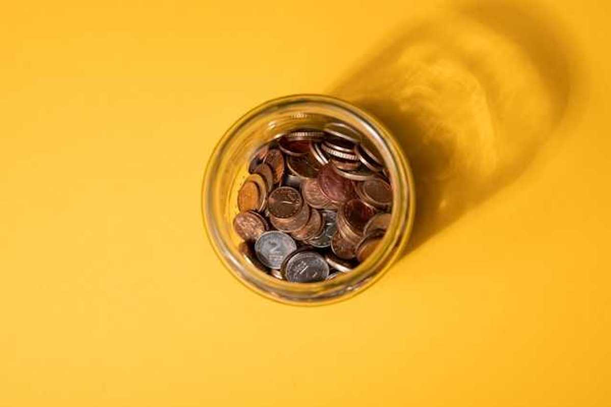 An overhead view of a jar of coins on a yellow background