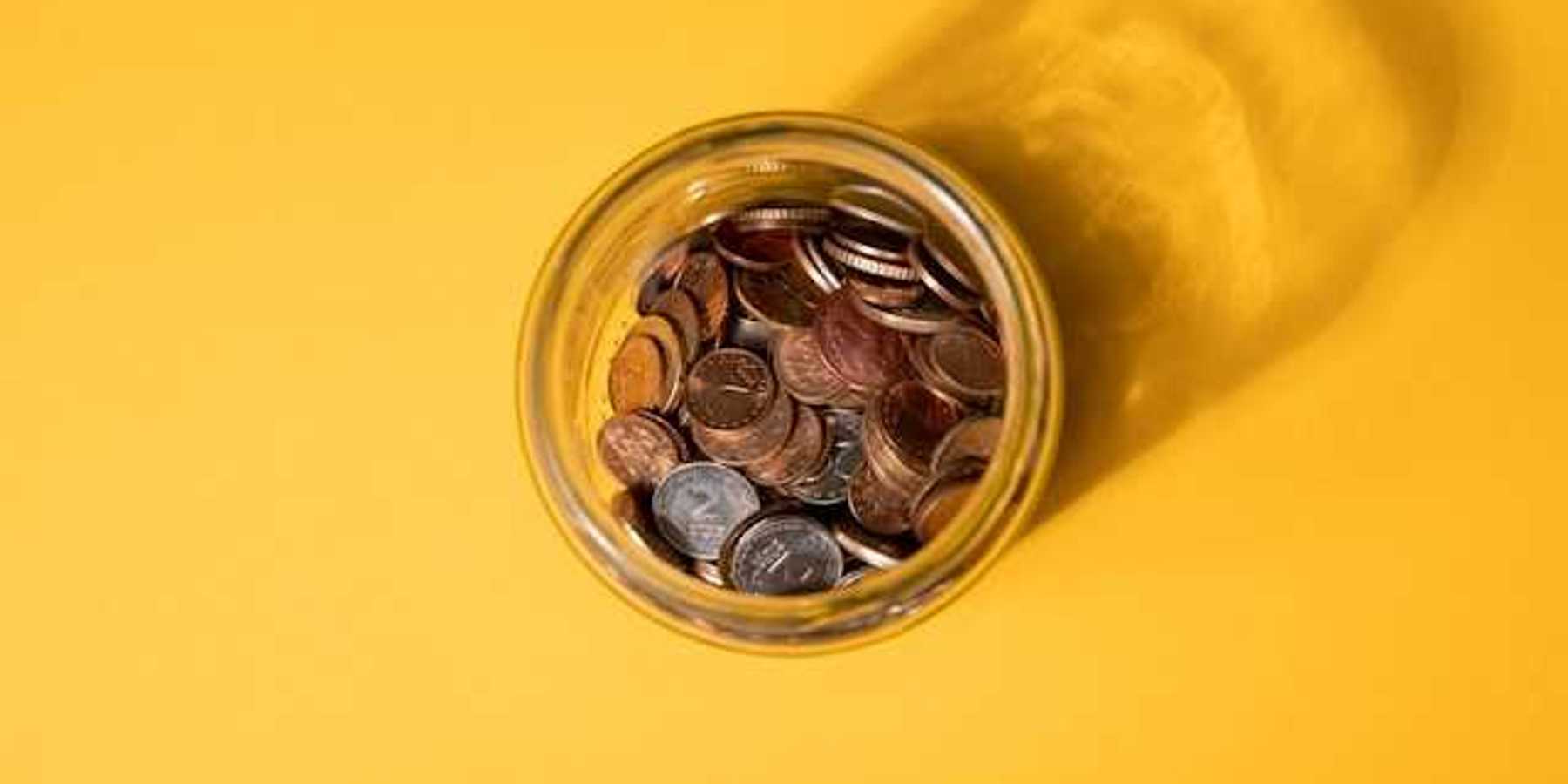 An overhead view of a jar of coins on a yellow background