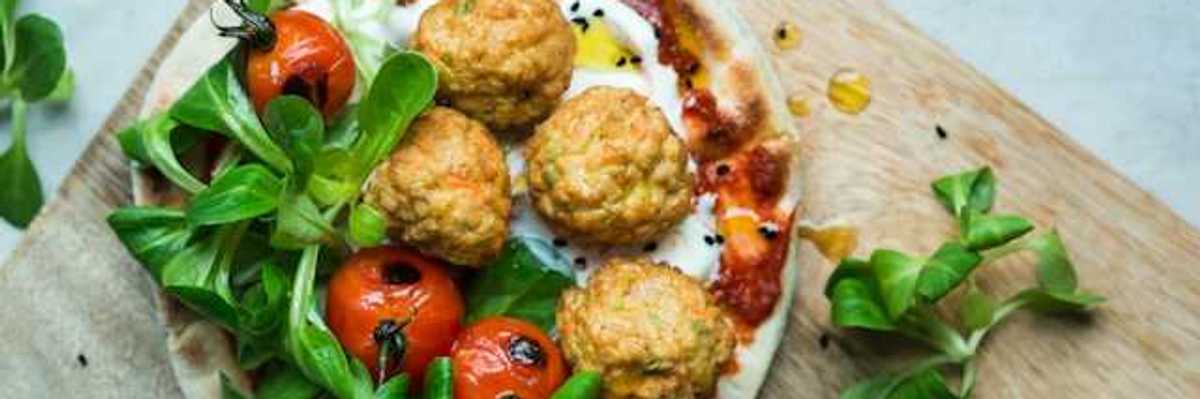 An overhead view of a plate of plant based meatballs and tomatoes on pizza dough