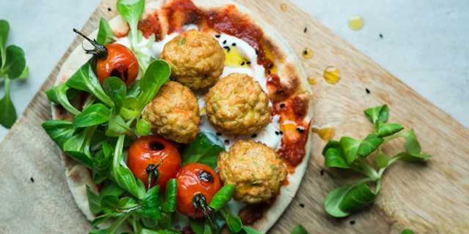 An overhead view of a plate of plant based meatballs and tomatoes on pizza dough