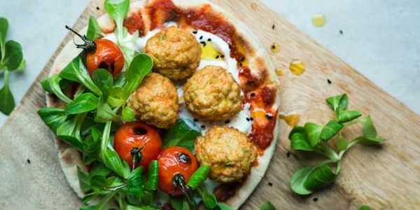 An overhead view of a plate of plant based meatballs and tomatoes on pizza dough