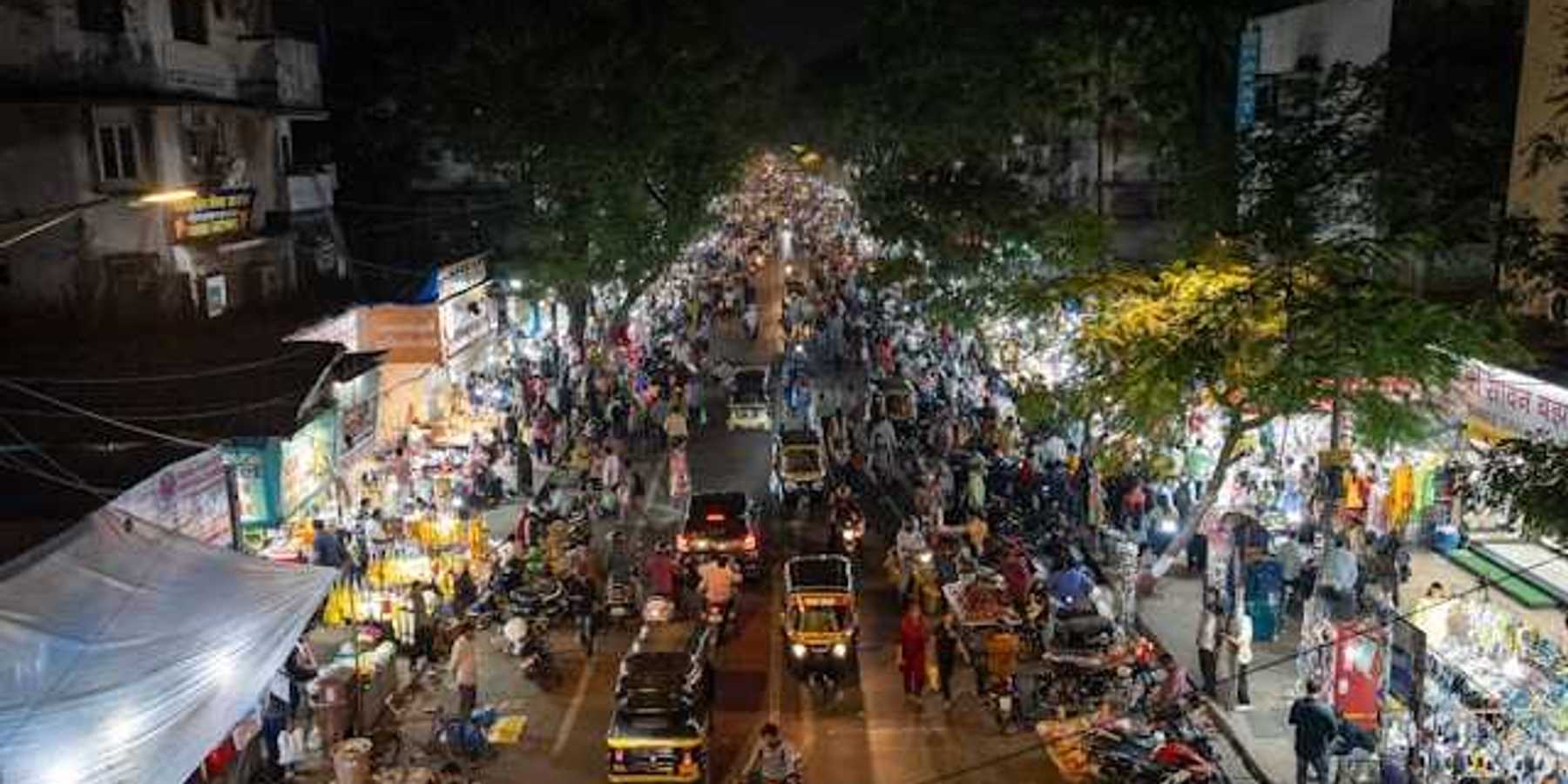 An overhead view of a street in Mumbai, India at night filled with cars, people, and shop entrances