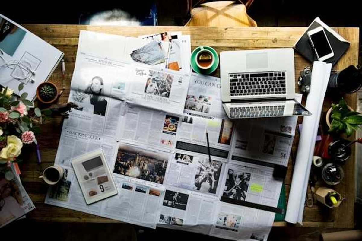 An overhead view of a table with a newspaper, a tablet, and a laptop on it