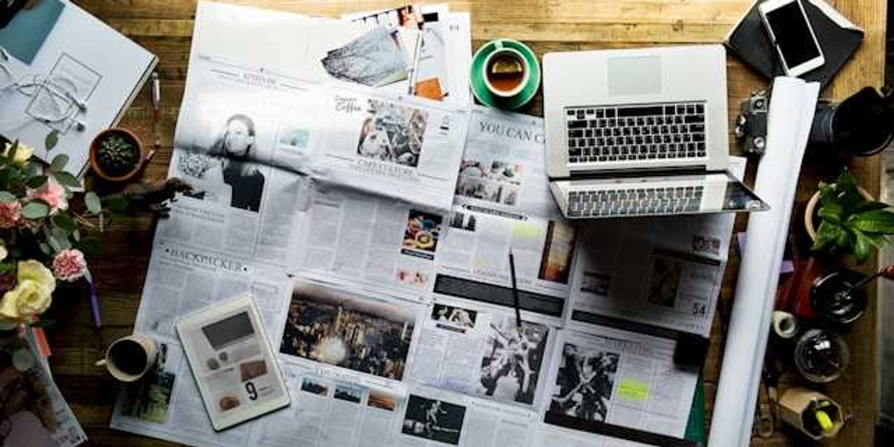 An overhead view of a table with a newspaper, a tablet, and a laptop on it