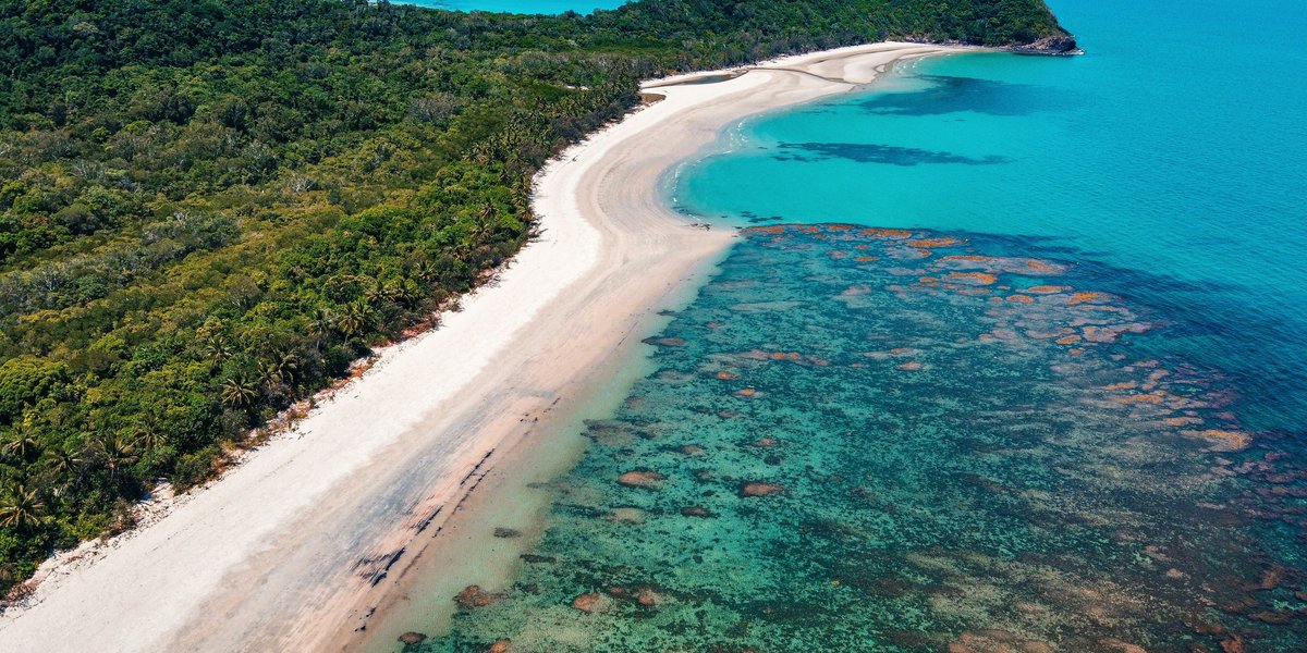 An overhead view of the Great Barrier Reef and forested coastline.