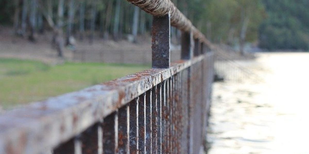 An oxidized fence running along a flooded river.