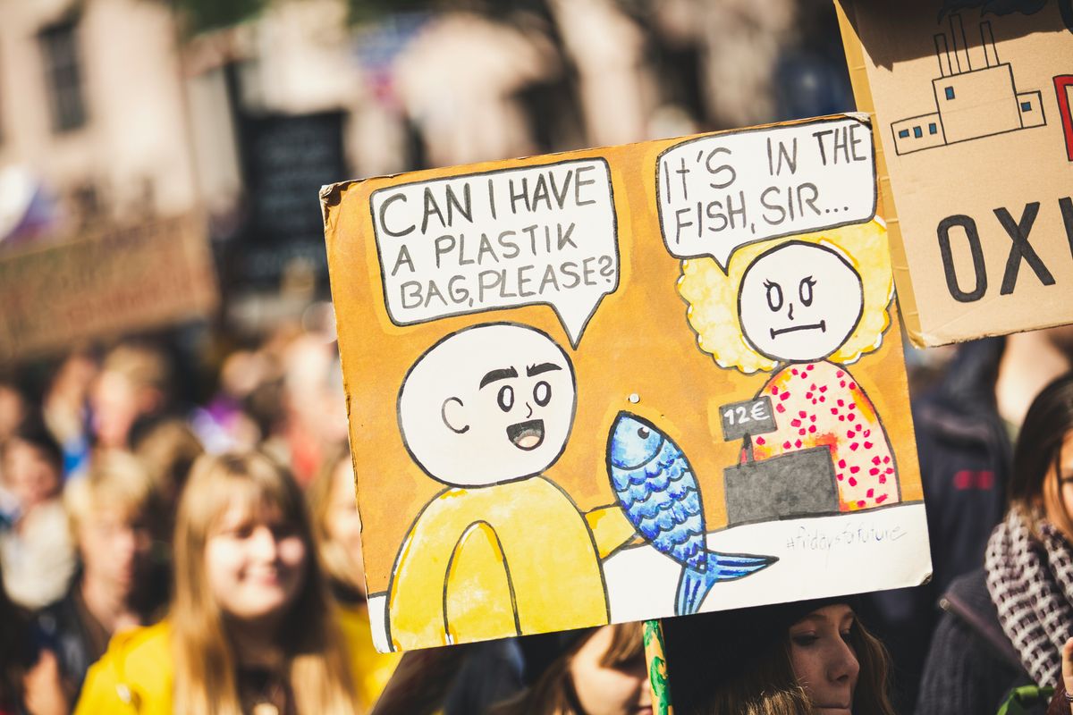 An protester holding a sign with a cashier telling a customer that their plastic bag is in the fish they're buying