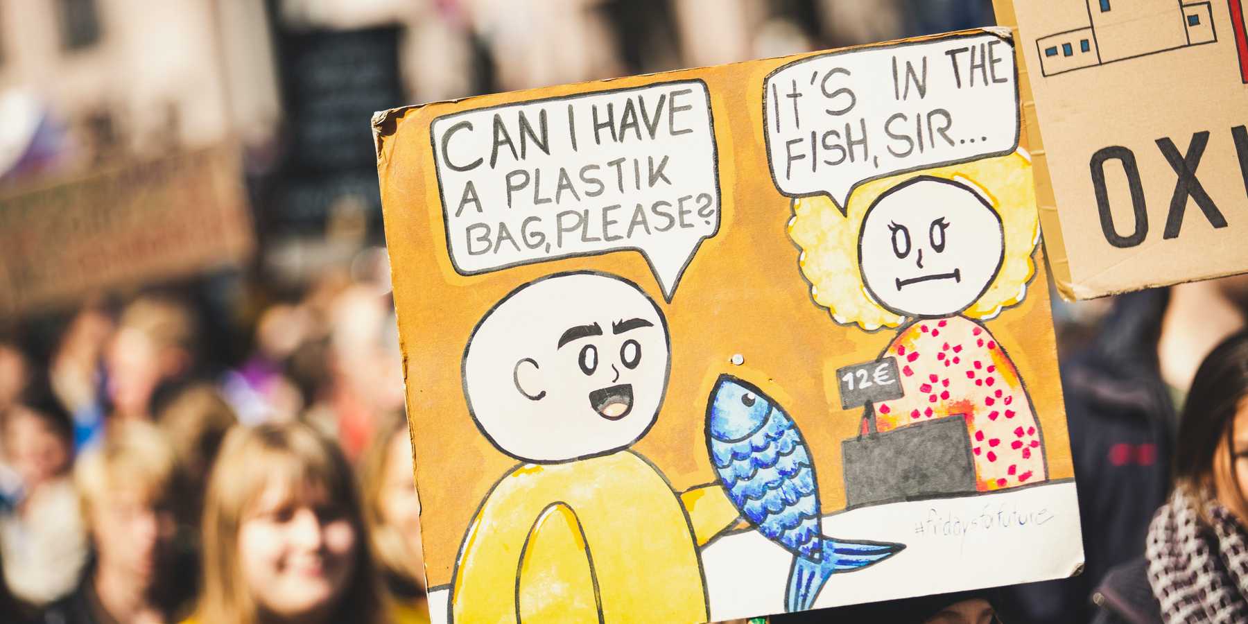 An protester holding a sign with a cashier telling a customer that their plastic bag is in the fish they're buying