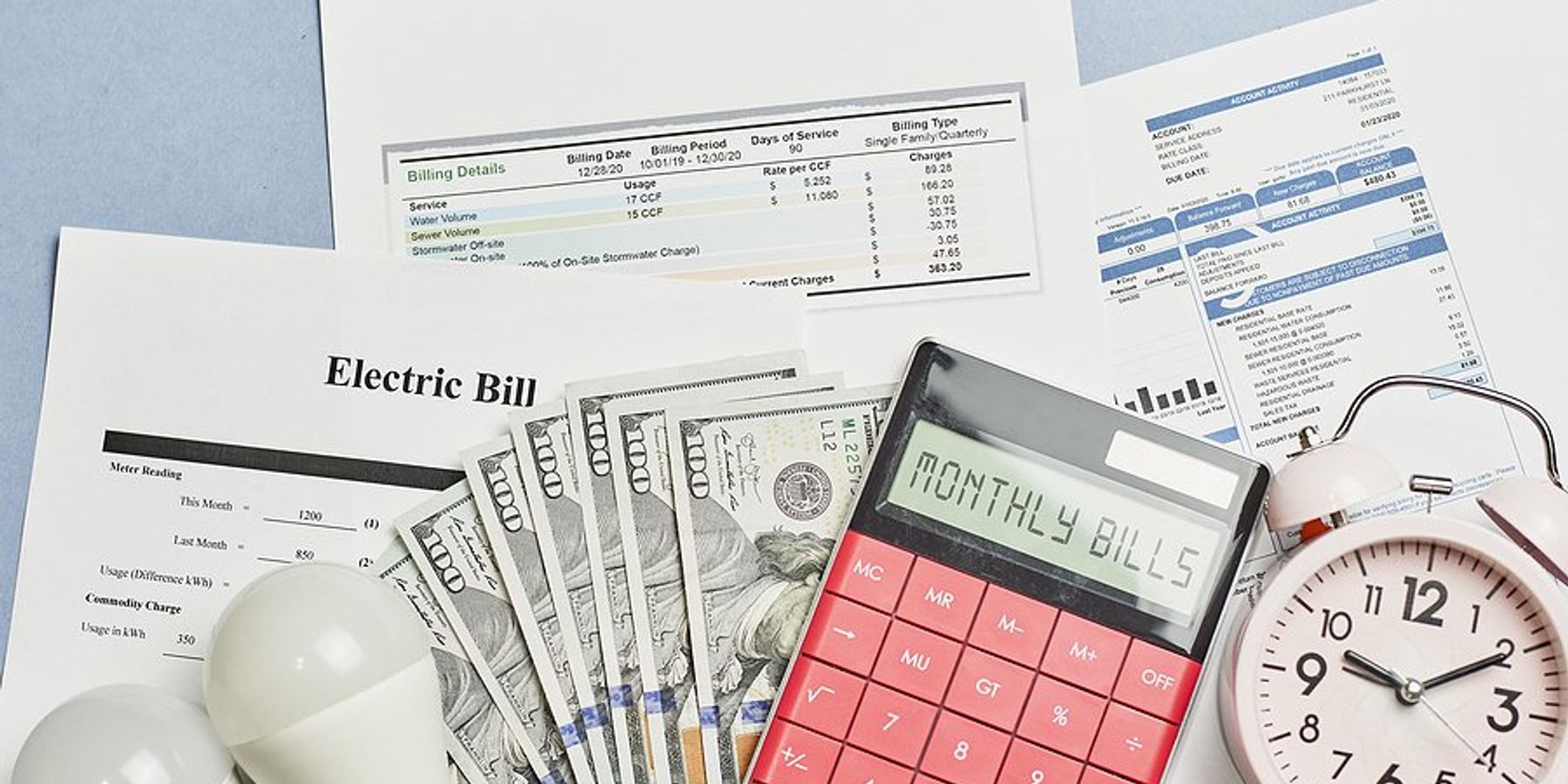 Assorted utility bills with cash, a calculator, and a timer on top of them.