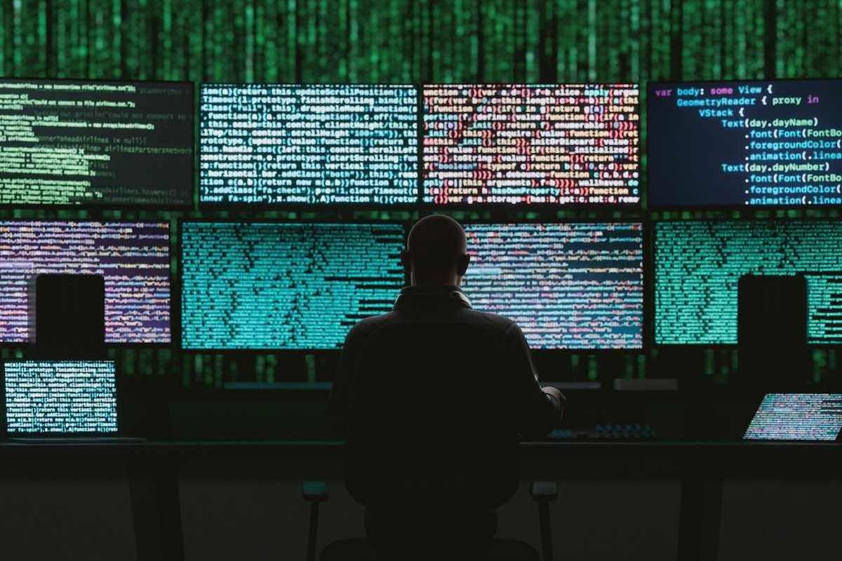 Back of a seated person monitoring data and digital code on multiple monitors