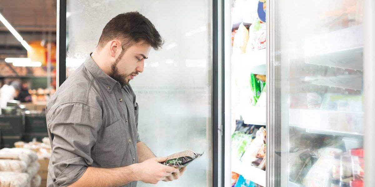 Bearded man with frozen food in his hands stands at the refrigerator in the department of frozen food.