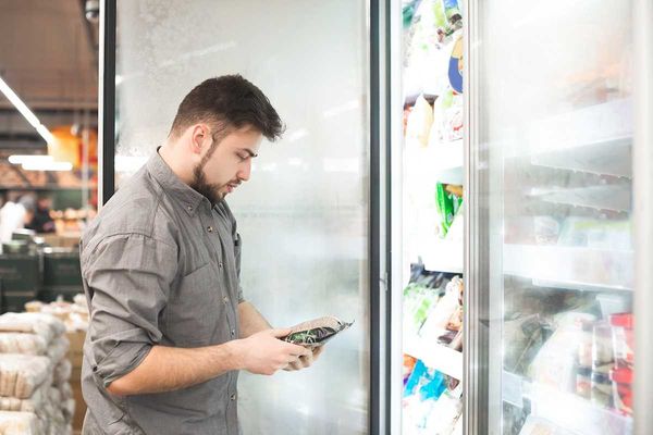 Bearded man with frozen food in his hands stands at the refrigerator in the department of frozen food.