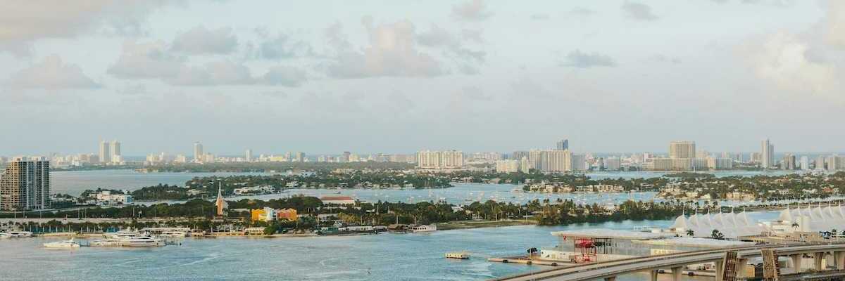 Biscayne Bay, Florida. MacArthur Causeway arches over the tranquil water, connecting to a vibrant marina brimming with yachts. In the distance, the iconic Miami Beach skyline.