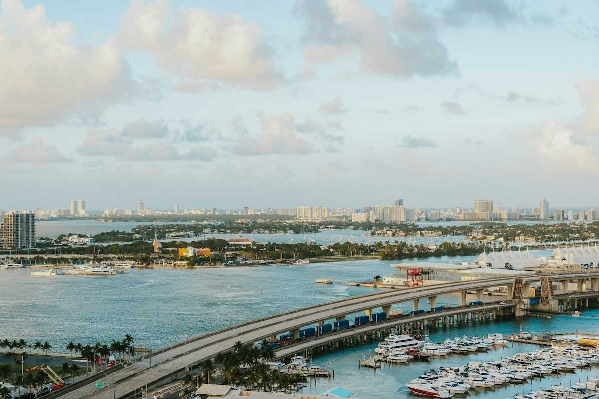 Biscayne Bay, Florida. MacArthur Causeway arches over the tranquil water, connecting to a vibrant marina brimming with yachts. In the distance, the iconic Miami Beach skyline.