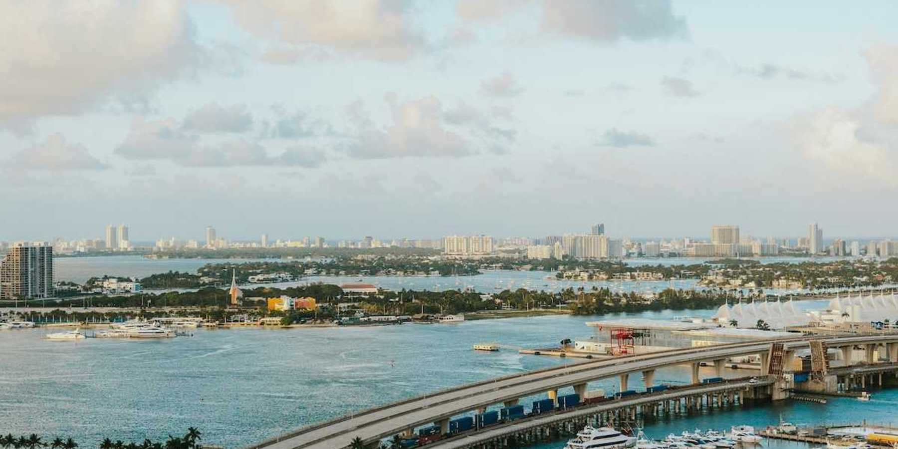 Biscayne Bay, Florida. MacArthur Causeway arches over the tranquil water, connecting to a vibrant marina brimming with yachts. In the distance, the iconic Miami Beach skyline.