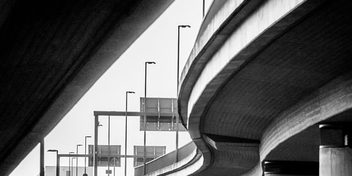 Black and white photo of a highway view of an overpass from below.