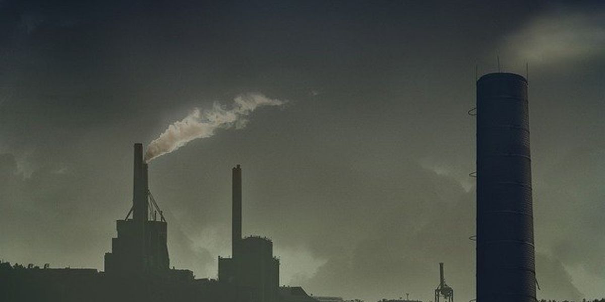 Black and white photo of smoke stacks emitting smoke.