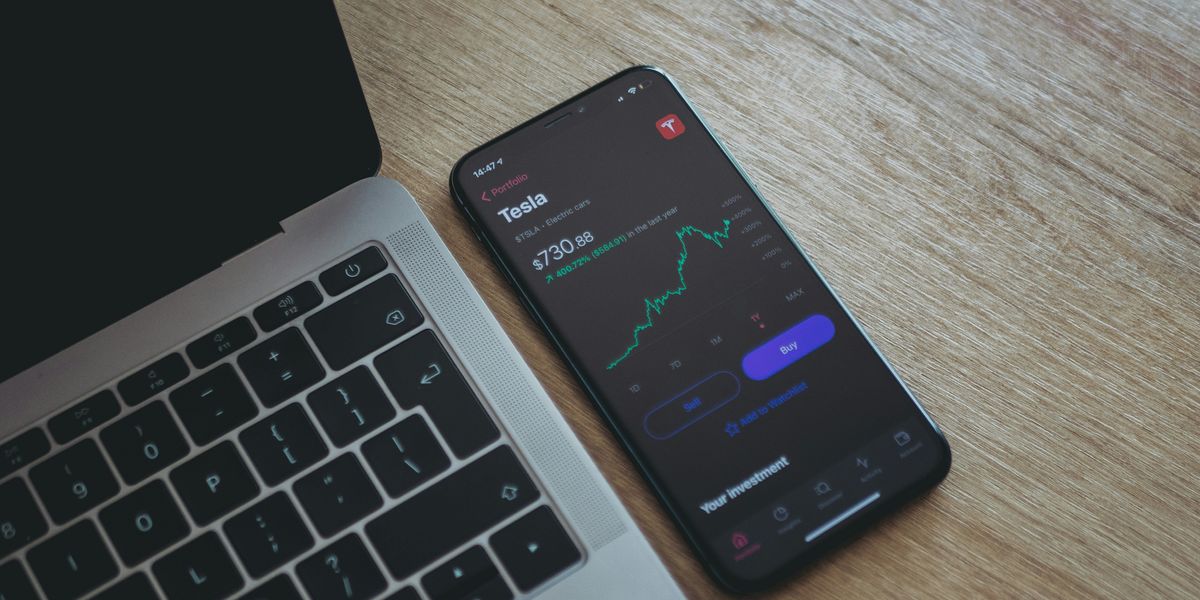 black android smartphone showing Tesla stock screen next to macbook pro.