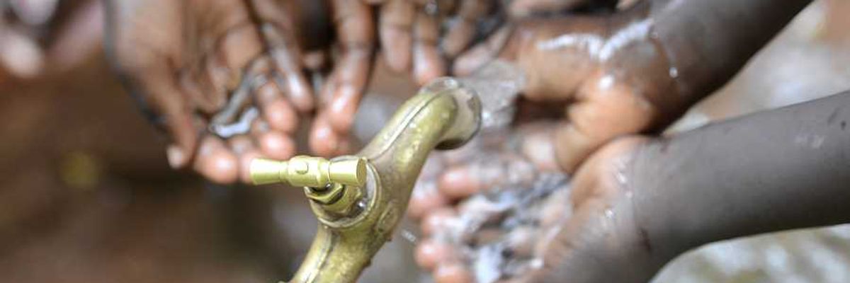 Black children holding their hands under a faucet with water coming out of it