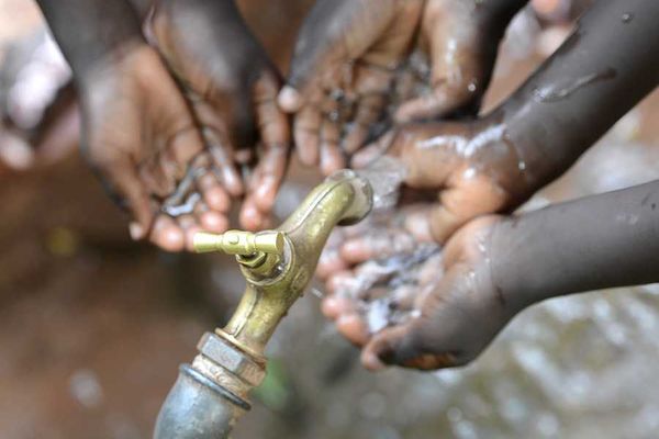 Black children holding their hands under a faucet with water coming out of it